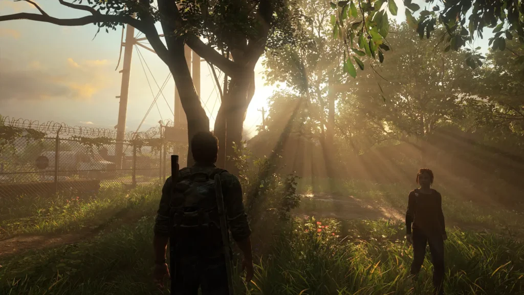 Screenshot aus The last of Us Part 1: Zwei Charaktere in einer sehr atmosphärischen Gegend. Ein Baum ist zu sehen so wie Joel und Ellie. Zwischen den Blättern der anderen Bäumen scheint die Sonne durch.